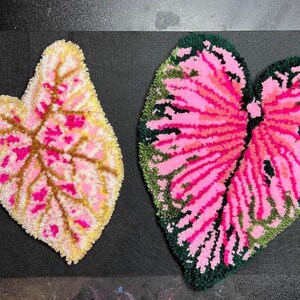 May include: Two handmade leaf-shaped rugs. One is a light yellow and pink color, and the other is a heart-shaped leaf with pink and green colors. The rugs are made with a tufting technique.