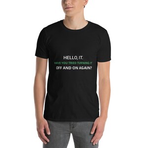Può includere: T-shirt nero con la scritta "HELLO, IT. HAVE YOU TRIED TURNING IT OFF AND ON AGAIN?" in bianco e verde. La maglietta è a maniche corte e girocollo.