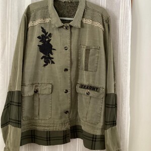 May include: Olive green jacket with black rose embroidery and "US ARMY" text on the pocket. Features a plaid pattern on the sleeves and hem, with decorative stitching on the shoulders. The jacket has multiple pockets and button closures.
