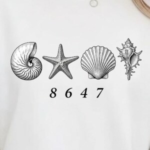 Op de afbeelding: Wit T-shirt met een zwart-wit ontwerp van schelpen en een zeester, met de nummers 8647 eronder gedrukt. Het ontwerp is gecentreerd op het shirt.