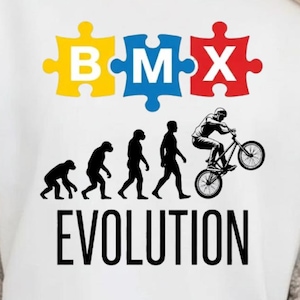 Peut inclure: T-shirt blanc avec un motif sur le thème du BMX. Le motif comprend le mot "BMX" en lettres de puzzle et un graphique de l'évolution humaine se terminant par une personne faisant du vélo BMX. Le mot "EVOLUTION" est imprimé en dessous.