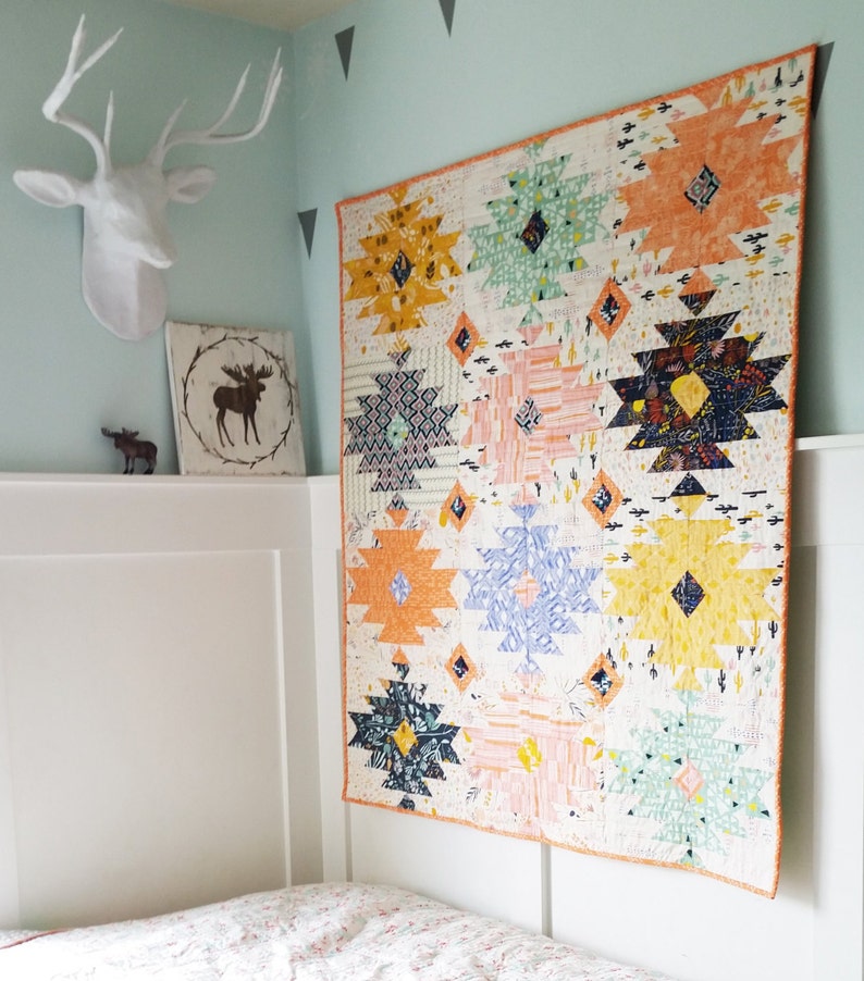 Puede incluir: Una colcha colorida con un patr&oacute;n geom&eacute;trico en tonos de naranja, amarillo, azul, verde y blanco. La colcha est&aacute; colgada en una pared blanca en una habitaci&oacute;n con un techo blanco y paredes de color azul claro.