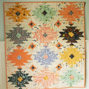 Puede incluir: Una colcha colorida con un patr&oacute;n geom&eacute;trico de estrellas y diamantes. La colcha est&aacute; hecha de varias telas en tonos de naranja, amarillo, verde, azul y negro. La tela de fondo es blanca con un peque&ntilde;o estampado de cactus.
