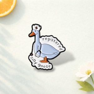 Op de afbeelding: Een grillige emaille pin met een cartoon gans met een verpleegsterspet en stethoscoop. De pin is lichtblauw en wit met de woorden "registered silly goose". De pin heeft een zwarte omtrek.