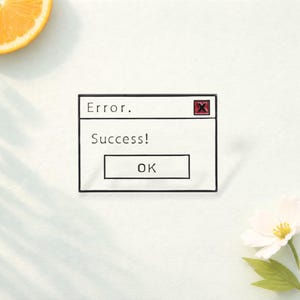 Puede incluir: Un pin de esmalte rectangular que muestra un cuadro de diálogo de computadora blanco con un borde negro. El texto dice Error. en la parte superior, Success! en el centro y OK dentro de un botón. Un pequeño cuadrado rojo con una X negra está arriba.