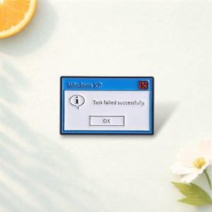 Op de afbeelding: Blauw-witte emaille pin in de vorm van een Windows XP foutmelding. De pin toont de tekst "Windows XP", de melding "Task failed successfully." en een "OK" knop. Een rode "X" staat in de rechterbovenhoek.