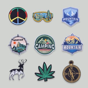Può includere: Una collezione di toppe ricamate con vari disegni. Include un simbolo di pace, scene di montagna, tema campeggio, un cervo, una foglia di cannabis e una bussola. Le toppe presentano colori vivaci e cuciture dettagliate.