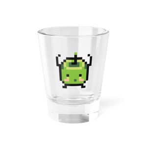 Puede incluir: Un vaso de chupito transparente con un diseño de manzana verde pixelada. El personaje de la manzana tiene los brazos levantados. El vaso de chupito es cilíndrico y está sobre una superficie blanca. El personaje de la manzana tiene una expresión linda.