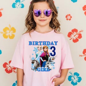 Może przedstawiać: Dziewczynka w r&oacute;żowej koszulce z grafiką z filmu Kraina Lodu i niebieskim napisem "BIRTHDAY 3 GIRL". Ma r&oacute;wnież okulary przeciwsłoneczne w kształcie serca. Tło przedstawia wz&oacute;r kwiatowy.