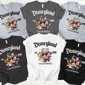May include: A collection of t-shirts in various colors, including gray, black, and white. Each shirt features the Disneyland logo with the text "est. 1955" and a graphic of Disney characters. The word "CALIFORNIA" is also printed on the shirts.
