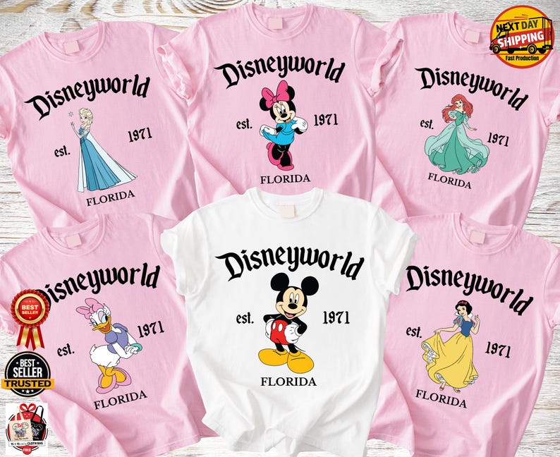 Op de afbeelding: Roze en witte T-shirts met Disney-personages en de tekst "Disneyworld est. 1971 Florida." Elk shirt heeft een ander personage: Elsa, Minnie Mouse, Ariel, Katrien Duck, Mickey Mouse en Sneeuwwitje.