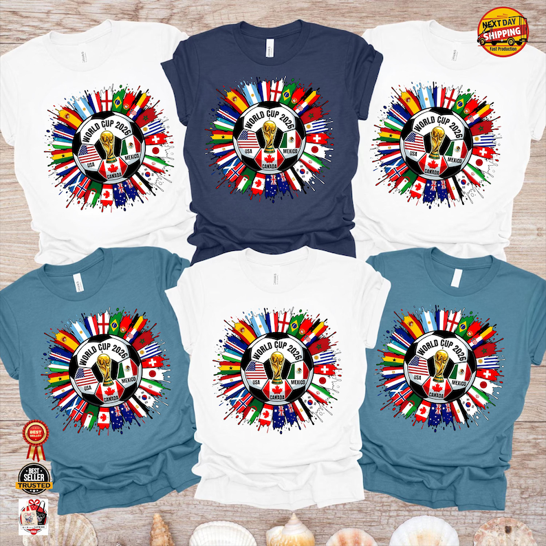 May include: A collection of t-shirts in various colors, each featuring a soccer ball design with the text "WORLD CUP 2026". The design includes flags of different countries and a trophy. The shirts are white, navy blue, and teal.