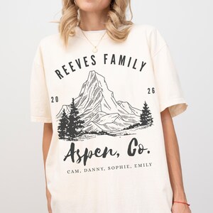 Pu&ograve; includere: T-shirt color crema con grafica di montagna nera e la scritta "REEVES FAMILY Aspen, Co." con nomi e date. La maglietta ha maniche corte e una vestibilit&agrave; ampia.