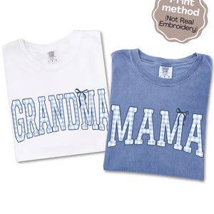 May include: A white t-shirt with the word GRANDMA and a blue t-shirt with the word MAMA, both featuring blue and white gingham block lettering with a small bow graphic on the final letter. A badge states Print method (Not Real Embroidery).