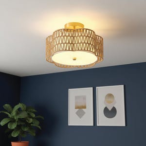 May include: A flush mount ceiling light fixture with a woven, natural-toned shade. The light has a gold-colored base and a white, frosted glass diffuser. The fixture is mounted on a white ceiling in a room with navy blue walls.
