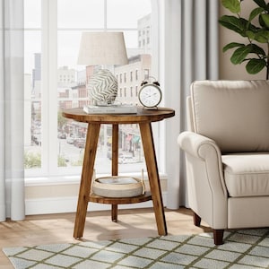 May include: A round, wooden side table with a lower shelf and three angled legs. A lamp with a beige shade, a decorative vase, and a clock sit on top. The table is approximately 24 inches in diameter.