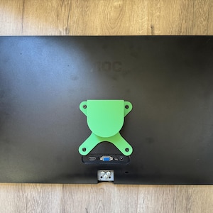 Op de afbeelding: Een zwarte AOC-monitor met een felgroene montagebeugel aan de achterkant. De monitor heeft verschillende poorten en connectoren aan de onderkant. De monitor ligt op een lichtbruin houten oppervlak.