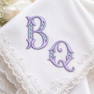 May include: White handkerchief with delicate lace trim and embroidered lavender letters "B" and "Q". The letters have a teal accent. The handkerchief is likely for a wedding or special occasion.
