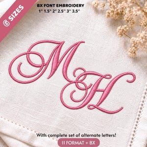 Op de afbeelding: Een roze geborduurd monogram van de letters M en H in cursief schrift op een witte stoffen achtergrond. De tekst bevat 6 SIZES, BX FONT EMBROIDERY 2,5cm 3,8cm 5cm 6,3cm 7,6cm 8,9cm, en With complete set of alternate letters! 11 FORMAT + BX.