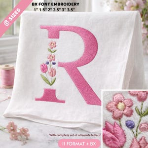 Peut inclure: Tissu blanc avec une grande lettre "R" brodée en rose, ornée de motifs floraux. La broderie comprend des fleurs roses, des feuilles vertes et de petits accents violets. Le texte "BX FONT EMBROIDERY" et les tailles sont visibles.