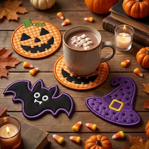 Puede incluir: Un juego de tres posavasos de tela que incluyen una calabaza con cara de jack-o'-lantern, un murciélago negro con ojos blancos y un sombrero de bruja morado con una hebilla amarilla, dispuestos alrededor de una taza de cerámica.