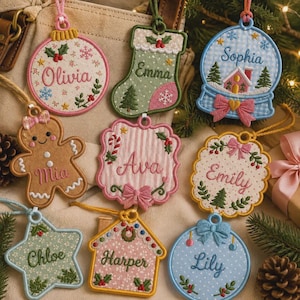 May include: A collection of eight embroidered fabric Christmas ornaments in various shapes including a round bauble, stocking, snow globe, gingerbread person, scalloped plaque, star, and house, each featuring a unique name and festive motifs.