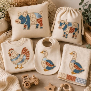 May include: A collection of cream-colored textile items featuring patchwork-style animal appliqués. Included are a square pillow with a pig, a drawstring bag with a cow, a long-sleeve shirt with a chicken, a bib with a duck, and a towel with a duck.