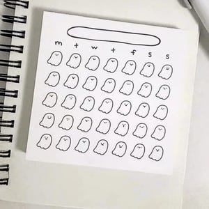 May include: A square white sticky note featuring a black ink grid of thirty-five small ghost illustrations arranged in five rows of seven. Above the ghosts, the letters m, t, w, t, f, s, s are printed in a row, with an empty oval outline above them.