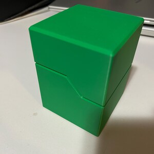 May include: A bright green, two-piece box with a square shape. The top section sits atop the bottom section, with a diagonal cut on the side. The box is made of a solid, opaque material.