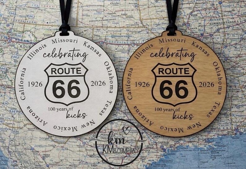 Peut inclure: Deux ornements circulaires Route 66. L'un est blanc, l'autre est en bois clair. Ils pr&eacute;sentent l'&eacute;cusson Route 66, les ann&eacute;es 1926 et 2026, et l'inscription "100 years of kicks". Suspendus par des cordons noirs.