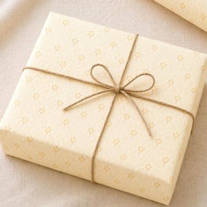 Golden yellow floral wrapping paper wrapped gift styled on a soft linen background with twine bow, warm aesthetic gift wrap for birthdays and gifts for her