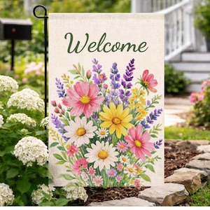 Puede incluir: Una bandera de jardín con la palabra "Welcome" en escritura verde. La bandera presenta un diseño floral de acuarela con flores rosas, amarillas, moradas y blancas. La bandera se exhibe en un jardín.