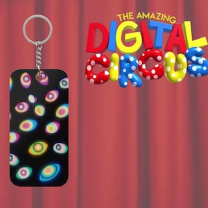 Puede incluir: Un llavero rectangular negro con una cadena y un anillo plateados. El llavero presenta un patrón de ojos coloridos y estilizados. Las palabras "THE AMAZING DIGITAL CIRCUS" se muestran en letras de burbujas 3D coloridas.