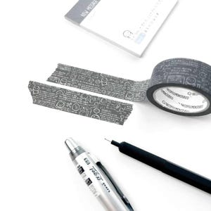 May include: A roll of dark gray washi tape with a repeating pattern of white cartoon faces and text, with two torn pieces of the same tape. A silver pen and a black pen are also visible, along with a notepad that says "NEW MESSAGE".