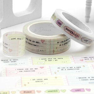 May include: Washi tape rolls in pastel shades with handwritten text and illustrations. The tape includes phrases such as "Notes" and "List", along with hearts and other small designs. Ideal for journaling and craft projects.