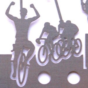 May include: Silhouette of three people riding bicycles. The person in the front is raising their arms in victory. The image is cut out of gray paper.