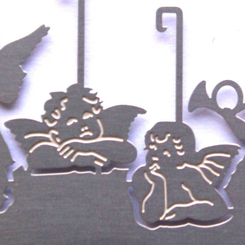 May include: A set of three metal angel ornaments with a hanging loop. The angels are in a sleeping pose with their wings outstretched. The ornaments are a light gray color.