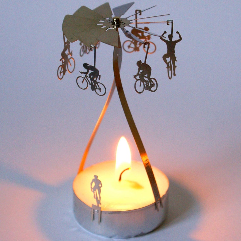 May include: A silver candle holder with a rotating carousel of cyclists. The carousel is powered by a tea light candle. The candle holder is made of metal and has a silver finish.