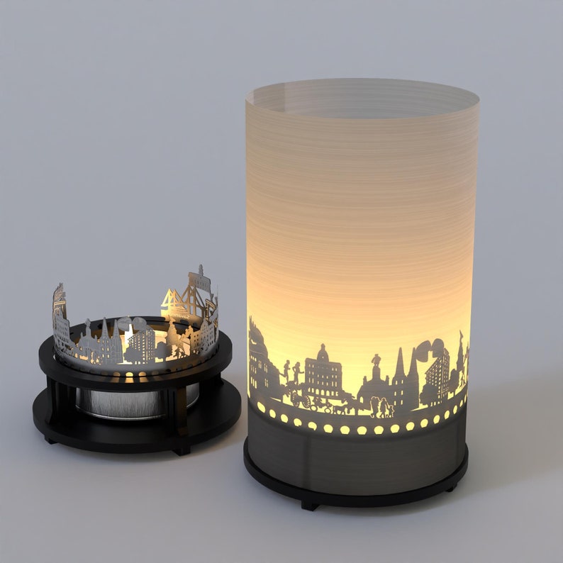 May include: A black metal candle holder with a cityscape silhouette design. The candle holder is lit and the light shines through the cutouts in the metal.