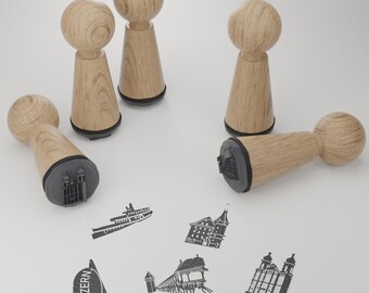 May include: Five wooden stamps with black ink pads. The stamps feature various designs, including a boat, a building, a bridge, and a church. The stamps are arranged on a white surface.