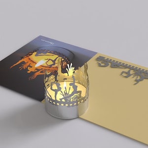 May include: A silver candle holder with a cutout design of people dancing. The candle holder is lit and casting a warm glow. The candle holder is on a yellow card with the text "The Present Company".