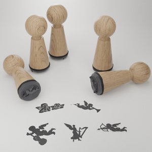 May include: Five wooden stamps with black ink pads, each featuring a different design of a cupid or cherub. The stamps are arranged on a white surface.