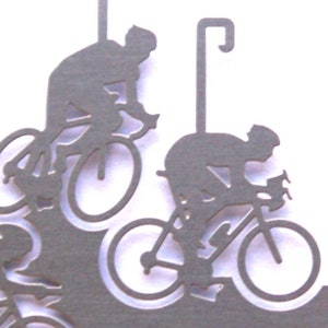 May include: A silver metal ornament featuring a silhouette of three cyclists riding bicycles. The ornament has a hook for hanging.