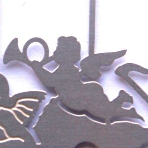 May include: A silver metal angel ornament with wings, playing a trumpet, riding a carousel horse. The ornament is a silhouette design.