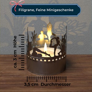 May include: A silver candle holder with a cutout design of yoga poses. The holder is 3 inches tall and 3.5 inches in diameter. The candle holder is on a wooden surface.