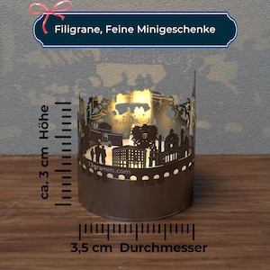 May include: A brown metal candle holder with a cut-out design of a city skyline. The candle holder is 3.5 inches in diameter and 3 inches tall. The text "Filigran, Feine Minigeschenke" is at the top of the image.