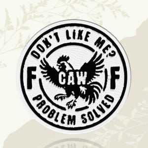 May include: A round, white embroidered patch with a black border. The patch features a black rooster graphic with the text "CAW" and the phrase "DON'T LIKE ME? PROBLEM SOLVED" in a circular design.