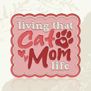 May include: Embroidered patch with the phrase "living that Cat Mom life" in red and white thread. The design includes a cat paw print with a heart, and two small hearts. The patch has a pink background and a scalloped border.