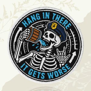 May include: Embroidered patch with a skeleton in a police hat drinking from a mug. The patch reads "HANG IN THERE" and "IT GETS WORSE" in blue and white. The design includes a rock and roll hand gesture, all on a black circular background.