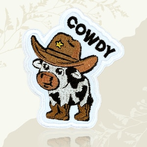 May include: Embroidered patch depicting a cartoon cow in a brown cowboy hat with a gold star. The cow has black and white spots and brown boots. The word "COWDY" is embroidered above the cow in black letters.